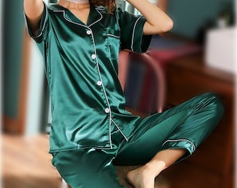 May include: A green satin pajama set with short sleeves and a button-up top. The top has a white trim and a pocket on the left side. The pants have a white trim along the legs.