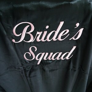 May include: Black satin robe with pink embroidery that reads "Bride's Squad".