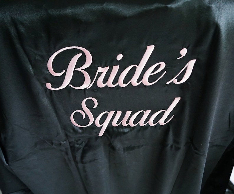 May include: Black satin robe with pink embroidery that reads "Bride's Squad".