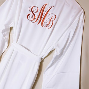 May include: White robe with a feather trim on the sleeves and a monogram of the letters "SMB" embroidered on the back in orange thread.
