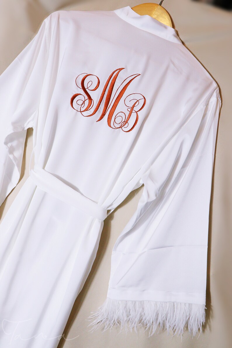 May include: White robe with a feather trim on the sleeves and a monogram of the letters "SMB" embroidered on the back in orange thread.