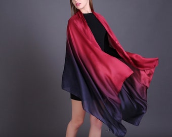 May include: A long, flowing scarf with a gradient of red to black. The scarf is made of a soft, silky material and is draped over a person's shoulders.