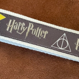 May include: White and gray Harry Potter themed key chain with a lightning bolt, the words "Harry Potter", and the Deathly Hallows symbol. The key chain has a silver metal ring.