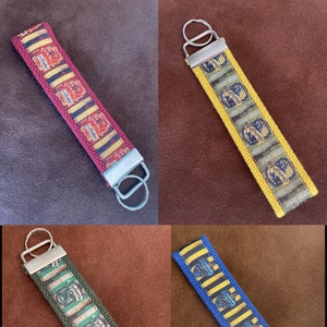 May include: Four different Harry Potter house keychains. Each keychain features a different house crest and colors: Gryffindor (red and gold), Hufflepuff (yellow and black), Slytherin (green and silver), and Ravenclaw (blue and bronze).