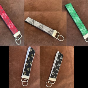 May include: Set of 6 keychains featuring a black and white, green, and red fabric with a repeating pattern of a triangle with a circle inside. The fabric has the text "Until the very end" printed on it. Each keychain has a silver key ring.