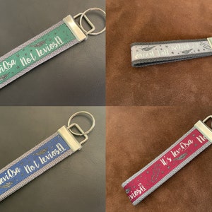 May include: Four different keychains with a gray fabric strap and a silver key ring. Each keychain has a different colored fabric strip with white text that reads "It's leviosa Not leviost" and a silver glitter design.