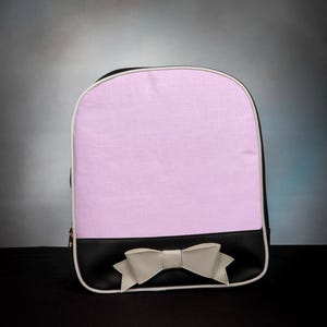 Könnte beinhalten: Ein rosa und schwarzer Rucksack mit einer weißen Schleife auf der Vorderseite.