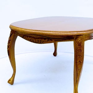 May include: A small, antique-style table with a light brown surface and ornate, curved legs. The legs are a darker shade of brown and feature detailed carvings. The table is approximately 12 inches long.