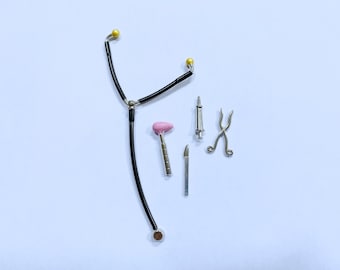 May include: Miniature medical tools including a stethoscope, a pink reflex hammer, a syringe, a scalpel, and forceps. The stethoscope is black with yellow earpieces. The tools are arranged on a white surface.