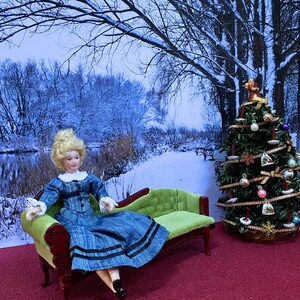 May include: A porcelain doll with blonde hair wearing a blue dress with black trim sits on a lime green miniature chaise lounge. Beside the lounge is a decorated Christmas tree with ornaments, ribbons, and a small angel topper.