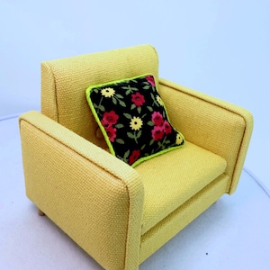 May include: A yellow armchair with a black and floral patterned pillow. The pillow has red and yellow flowers and green leaves.