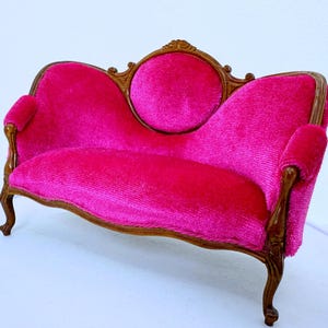 May include: A pink velvet loveseat with a carved wooden frame and ornate legs. The loveseat has a rounded back and a tufted seat.