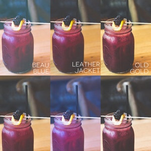 May include: Six mason jars filled with a dark purple liquid, garnished with a blackberry and a lemon twist. Each jar has a straw and a wooden skewer. The jars are arranged in two rows of three, with the names of each drink written below them: Beau Blue, Leather Jacket, Old Gold, Velvet Cake, Siberia Cold, and Wood Ash.
