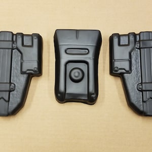 May include: Three black plastic pieces, possibly for a costume or prop. The pieces are shaped like a rectangle, a square, and a rectangle with a curved top.