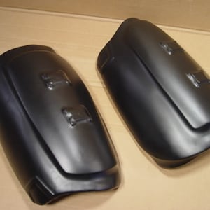 May include: A pair of black, moulded plastic shin guards with a smooth, matt finish. The guards have a curved shape and are designed to protect the shins and lower legs.