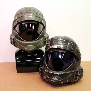 May include: Two green and black plastic helmets with visors. The helmets have a worn, distressed look, as if they have been used in battle.