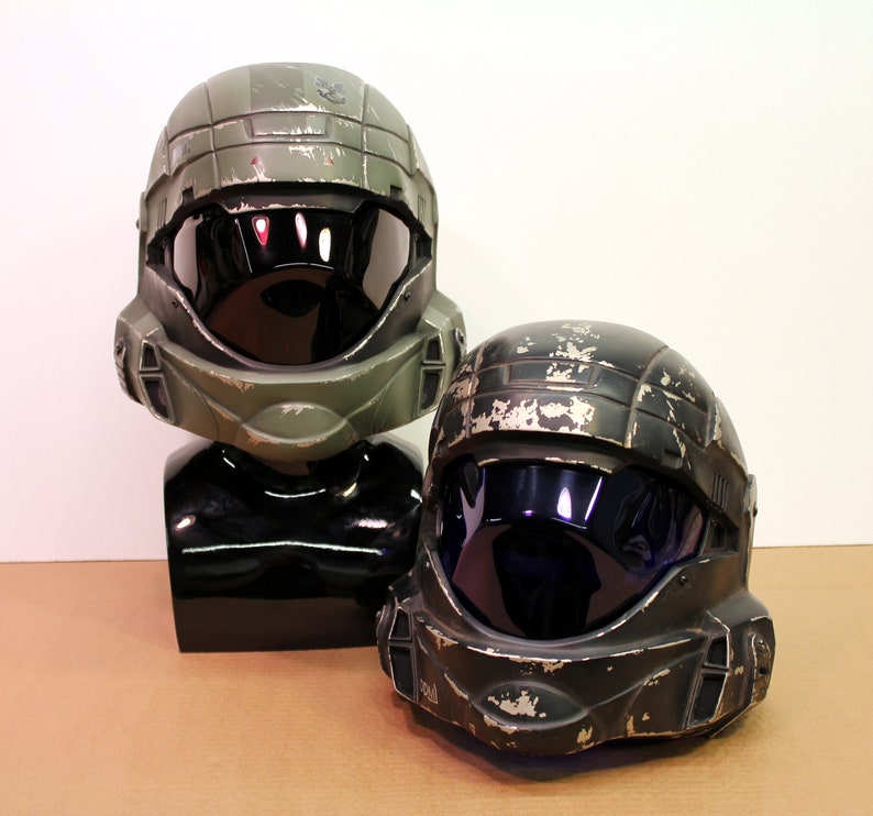 May include: Two green and black plastic helmets with visors. The helmets have a worn, distressed look, as if they have been used in battle.