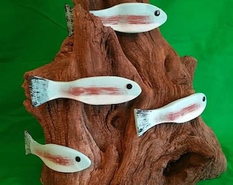May include: A wooden driftwood sculpture with four white and red painted fish attached to it. The driftwood is brown and has a rough texture. The fish are arranged in a staggered pattern, with the largest fish at the top and the smallest fish at the bottom.