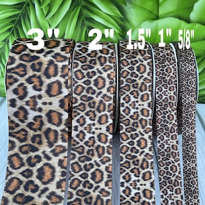 Peut inclure: Cinq bobines de ruban à imprimé léopard de différentes largeurs. Les largeurs sont étiquetées 3", 2", 1,5", 1" et 5/8". Le ruban présente un motif tacheté marron et beige sur fond noir. Le ruban est probablement utilisé pour l'artisanat et la décoration.