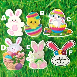 May include: A collection of colorful Easter-themed stickers. The stickers feature various designs, including a white bunny with pink accents, a chick hatching from an egg, and a bunny emerging from a cracked egg. Other stickers include a bunny with a basket of eggs and a bunny with a flower crown.