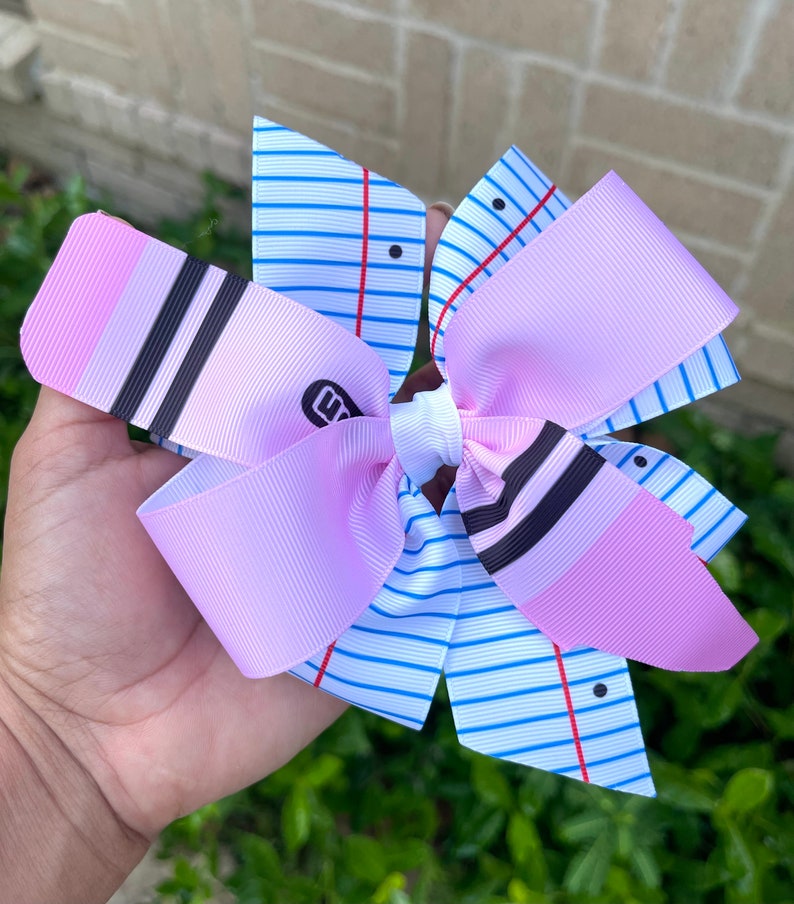 May include: A pink and white bow with a notebook paper design. The bow has black and white stripes and a pink and white striped design. The bow is tied with a white ribbon.