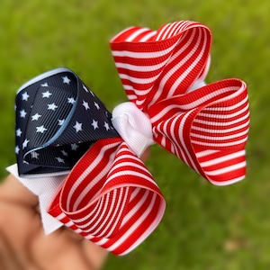 May include: A red, white, and blue bow with a star pattern. The bow is made of ribbon and is tied in a knot.