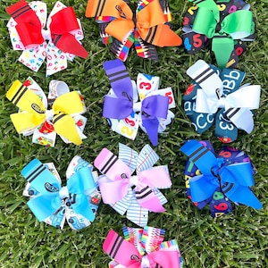 May include: Nine colorful hair bows with a school theme. The bows feature different patterns including crayons, pencils, numbers, letters, and school supplies.