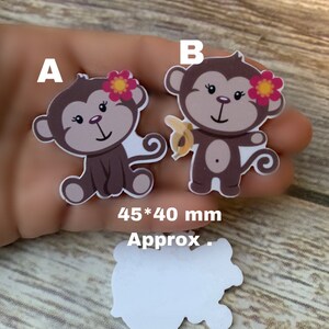 May include: Two brown monkey iron-on patches with pink flowers. The monkey on the right is holding a yellow banana. The patches are approximately 45 by 40 millimeters.