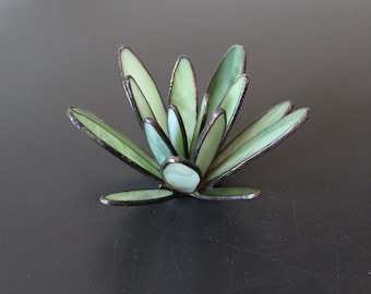 May include: A green glass succulent sculpture with a unique, modern design. The sculpture is made of many individual pieces of glass that are joined together to create a realistic-looking succulent.