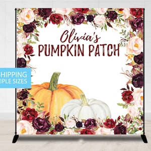 May include: A white backdrop with a burgundy floral border. The text "Olivia's Pumpkin Patch" is in the center of the backdrop. There are two pumpkins, one orange and one white, in the bottom center of the backdrop.