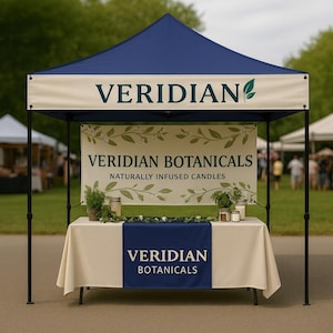 May include: A navy blue and cream-colored outdoor canopy tent with the text "VERIDIAN" and "VERIDIAN BOTANICALS NATURALLY INFUSED CANDLES". The table is covered with a cream-colored tablecloth and a navy blue table runner.