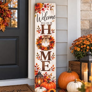 May include: A tall, rectangular wooden porch sign with a white-washed finish featuring the text Welcome TO OUR HOME. The letter O is replaced by an autumn wreath with a tan bow. The sign is decorated with orange, red, and yellow fall leaves.