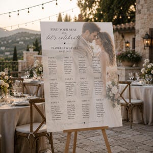 May include: A wedding seating chart sign on a wooden easel featuring a photograph of a couple, the text "FIND YOUR SEAT AND let's celebrate ISABELLA & JAMES 09.27.2025," and a list of twelve tables with guest names printed in a clear, dark font.