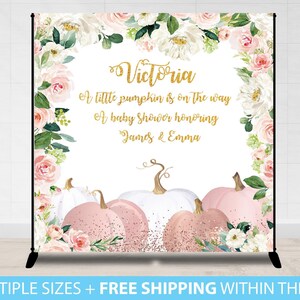 May include: A baby shower backdrop featuring a floral design with pink and white pumpkins. The backdrop includes the text "Victoria", "A little pumpkin is on the way", and "A baby shower honoring James & Emma". The backdrop is framed with white and pink flowers.