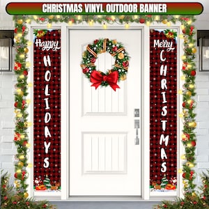 May include: Two red and black plaid Christmas banners with white snowflakes. The banner on the left says "Happy Holidays" and the banner on the right says "Merry Christmas". A red and green wreath with a red bow hangs on the white door behind the banners.
