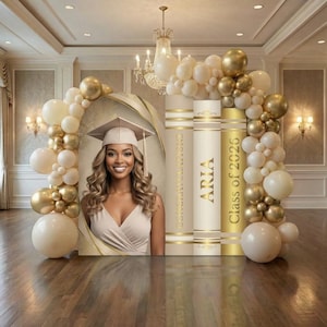 May include: A graduation backdrop featuring a portrait of a person in a cap and gown, alongside three large book-shaped panels labeled CONGRATULATIONS, ARIA, and Class of 2026. The display is framed by an arch of cream and metallic gold balloons.