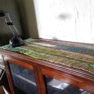 May include: A wooden cabinet with glass doors and a woven rug on top. The cabinet has a dark wood finish and the rug is a mix of brown, green, and blue colors.