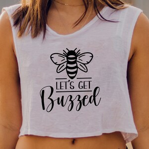 Könnte beinhalten: Weißes Crop-Top mit einer schwarzen Bienen-Grafik und dem Text "LET'S GET Buzzed". Das ärmellose Oberteil ist aus einem weichen Material gefertigt.