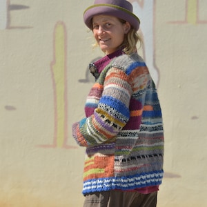Può includere: Un cardigan a righe colorate con un cappello viola. Il cardigan ha una varietà di colori, tra cui blu, verde, rosso, arancione e giallo.