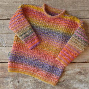 Può includere: Un maglione a righe colorate con collo rotondo. Il maglione è realizzato con una varietà di tonalità di arancione, rosa, viola e marrone.