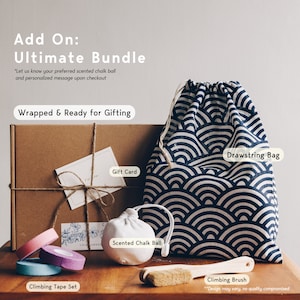 May include: A climbing bundle featuring a brown cardboard gift box with twine, a white gift card, a navy and white wave-patterned drawstring bag, a white scented chalk ball, a wooden climbing brush, and three rolls of climbing tape in pink, purple, and blue.