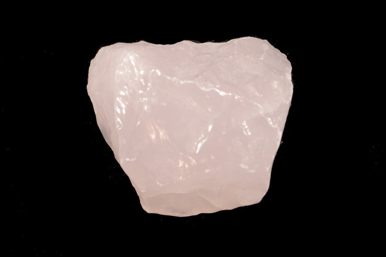 May include: A large, pale pink, rough-hewn rose quartz crystal.