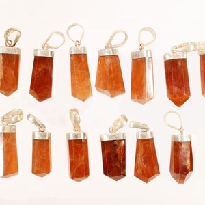 May include: A collection of orange-brown gemstone pendants with silver-colored metal caps and loops. The pendants are various shapes, including rectangular and faceted, and are approximately 1 to 2 inches in length. The background is white.