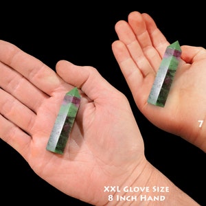 May include: Two hands holding green and pink gemstone points. The hand on the left is an adult hand with an 8 inch circumference. The hand on the right is a child's hand, 7 years old.
