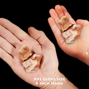 May include: Two hands holding a pile of rough, orange and white stones. The hand on the left is an adult hand with an 8 inch circumference. The hand on the right is a child's hand, 7 years old.