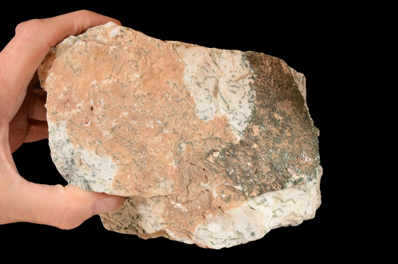 May include: A close-up of a light brown and green rock with a rough texture. The rock has a white, grey, and green marbling pattern.