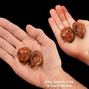 May include: Two red and black jasper tumbled stones in the palm of a hand wearing an XXL glove size 8 inch hand. Two more tumbled stones are in the palm of a 7 year old's hand.