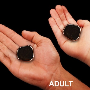 May include: Two hands, one adult and one of a 7-year-old child, hold a black, smooth, oval-shaped stone. The stone is slightly larger in the child's hand.