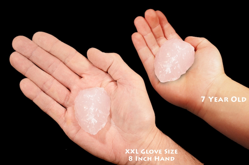 May include: Two hands holding a large, pink, translucent crystal. The hand on the left is an adult hand with an 8 inch circumference. The hand on the right is a child's hand, belonging to a 7 year old.