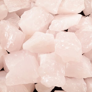 May include: A close-up of a pile of pink rose quartz crystals. The crystals are rough and have a natural, unpolished look.